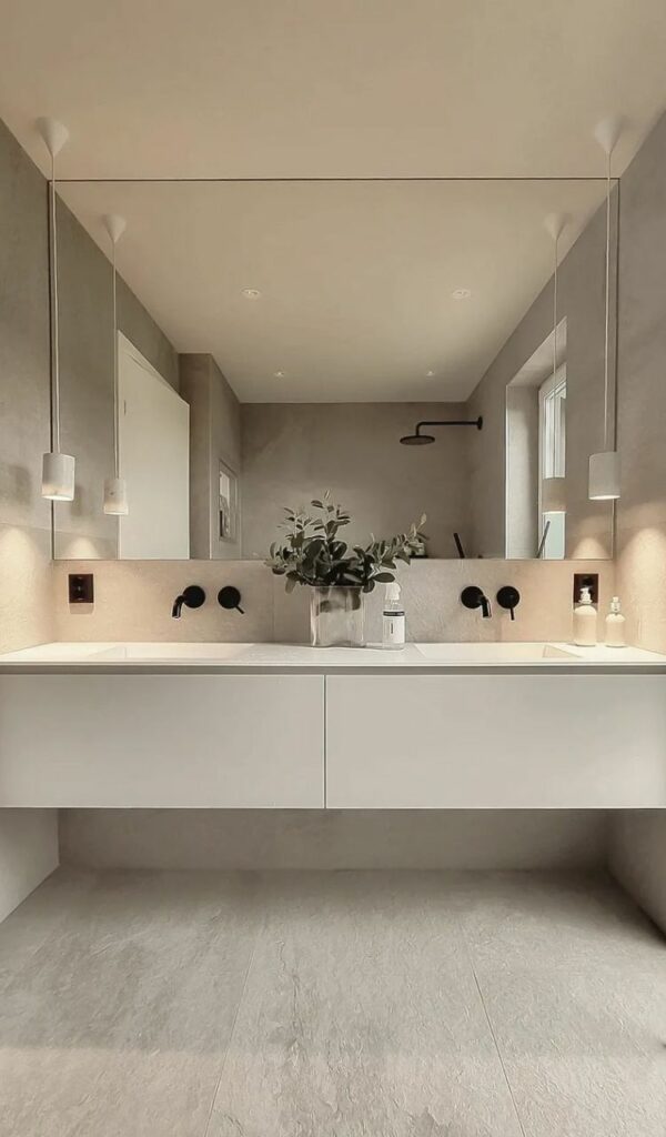 Dominato dai toni del beige e dal bianco, il bagno gioca sulla simmetria di lampade e lavabi